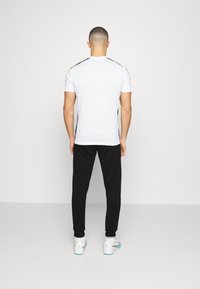 Witte sport T-shirt met zwarte accenten, gecombineerd met zwarte joggers en witte schoenen. De pasvorm is relaxed en legt de nadruk op comfort en mobiliteit.