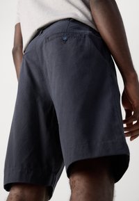 Pantaloni scurți bleumarin dintr-un amestec de bumbac, cu o textură netedă, buzunare laterale și un accent decorativ cu buton pe buzunarul din spate.
