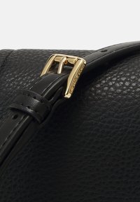 Borsa in pelle nera con finitura testurizzata. Presenta una fibbia color oro e una tracolla elegante per una lunghezza regolabile. Dettaglio del logo in rilievo di nota.