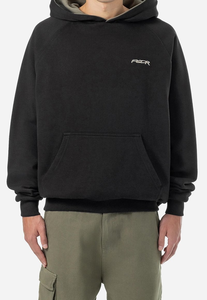 Homme portant un sweat à capuche noir avec une poche avant et un petit logo blanc sur la poitrine, associé à un pantalon cargo vert olive.
