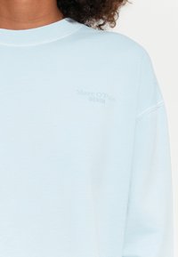 Felpa azzurra chiara realizzata in tessuto morbido, con collo rotondo e un logo Marc O’Polo Denim discreto sul davanti. Design e texture semplici.