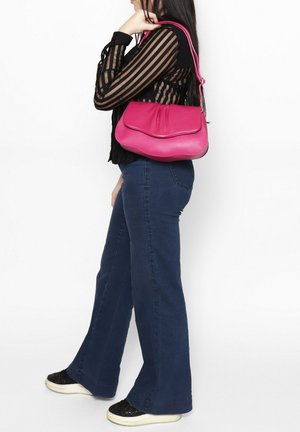 Sac à main en cuir rose avec un design incurvé, présentant une texture lisse et une fermeture à rabat. Porté de manière décontractée sur l'épaule, associé à un haut noir.