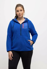 Sudadera de forro polar azul con un diseño de media cremallera, bolsillos tipo canguro y un bolsillo en el pecho con contraste azul y rojo. Tejido suave y texturizado.