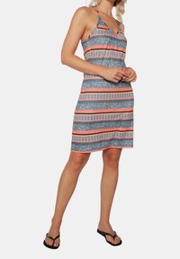 Robe à motif tropical en bleu marine avec des rayures corail et blanches, tissu léger, col en V et bretelles réglables. Accessoirisée avec des tongs noires.