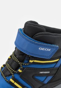 Modro-černá vysoká teniska se žlutými doplňky, s polstrovaným límcem, texturovanou tkaninou, zesílenou špičkou a suchým zipem.