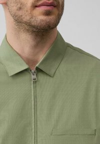 Lichtgroene ritshemd met kraag, voorzien van een voorzak en een gladde, geweven stof. Bevestigingsmateriaal omvat een zilveren rits.