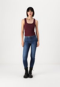 Débardeur bourgogne avec encolure carrée, associé à un jean bleu foncé ajusté et des bottes de combat noires à lacets. Design et texture simples.