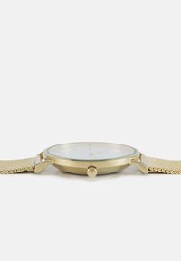Montre-bracelet dorée avec un bracelet en maille, un boîtier rond, un cadran blanc et une petite couronne. Présente des index horaires minimalistes et une surface en verre lisse.