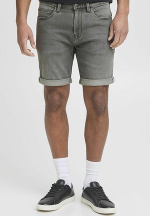 Graue Jeansshorts mit umgeschlagenen Säumen, Vordertaschen und einem taillierten Design. Das Modell kombiniert sie mit schwarzen Sneakers und weißen Socken.