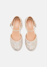 Zapatos de bailarina dorados con brillo, con una correa ajustable en el tobillo, puntera redondeada y un forro interior suave. Textura brillante y material suave.