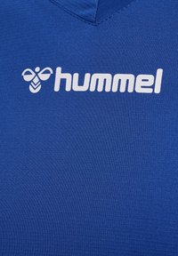 Blaues Sportshirt mit V-Ausschnitt, aus strukturiertem Stoff. Das "hummel"-Logo ist auffällig in Weiß auf der Brust angebracht.