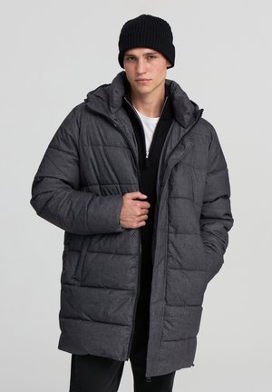 Giacca imbottita grigia con frontale con zip, cappuccio e tasche laterali. Tessuto testurizzato con motivo di trapuntatura orizzontale. Indossata sopra un top nero.