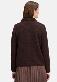 Braune, strukturierte Jacke mit Kragen, langen Ärmeln und lockerer Passform. Getragen über einem plissierten, taupefarbenen Rock.