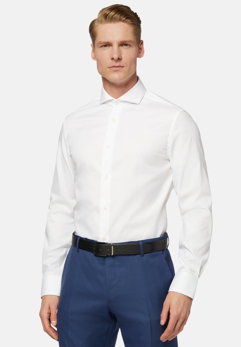 Weißes Langarmhemd mit klassischem Kragen, Button-Front und glatter Textur, kombiniert mit navyblauen Hosen und einem schwarzen Gürtel.