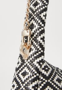 Sac en osier avec un motif géométrique noir et blanc, équipé d'un fermoir en métal doré et d'un détail en chaîne sur la poignée.