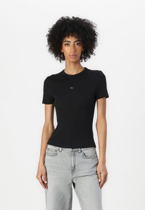 Maglietta nera attillata con maniche corte, scollatura tonda e discreto dettaglio del logo sul petto; abbinata a jeans in denim grigi chiari.