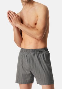 Boxers en coton rayés grisés avec une taille élastique et une fermeture à bouton unique à l'avant. Texture lisse avec des lignes verticales.