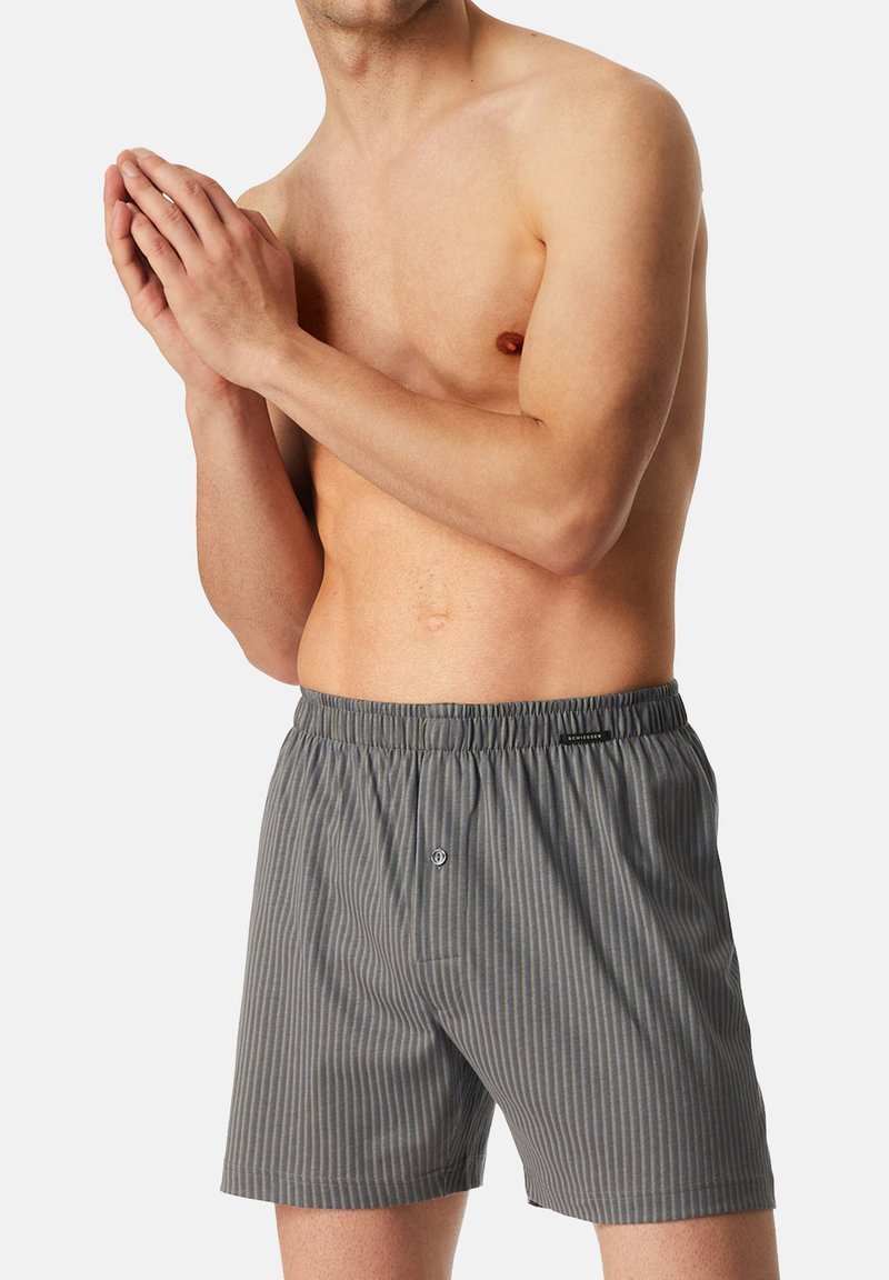 Boxers en coton rayés grisés avec une taille élastique et une fermeture à bouton unique à l'avant. Texture lisse avec des lignes verticales.