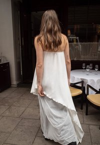 Biała, zwiewna sukienka bez rękawów o asymetrycznym dołku, wykonana z teksturowanej tkaniny. Gładka sylwetka i lekka konstrukcja.