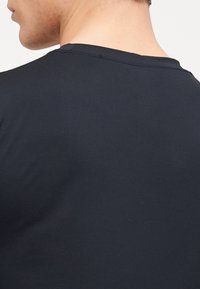 Czarny bawełniany T-shirt z gładką fakturą, okrągłym dekoltem i prostym, klasycznym designem. Bez wzorów ani widocznych elementów metalowych.