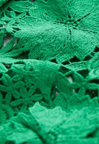 Textil croșetat verde cu modele florale detaliate, texturi variate și detalii brodate în relief. Designul este stratificat și tridimensional.