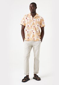Korte mouwen, lichtgekleurde shirt met een bloemmotief in wit en rood, gecombineerd met beige chino's en zwarte sandalen.