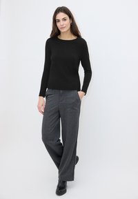Pull noir à manches longues avec un col rond et une texture en maille, associé à un pantalon gris coupe large et ajustée, doté de poches latérales et d'un motif subtil.