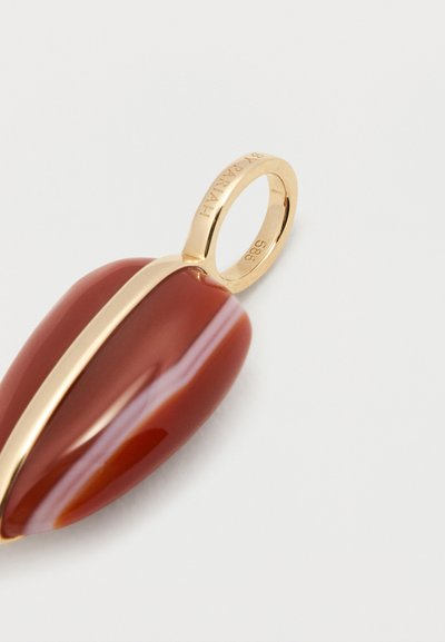 Arany medál, amely át van fűzve egy sima, csepp alakú, vörösesbarna kőn keresztül, arany csíkkal és gravírozott márkanévvel a medál karikáján.