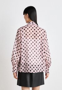 Lett, gjennomsiktig bluse i rosa med store svarte prikker. Har kragehals og lange, puffete ermer. Teksturert stoff, avslappet passform.