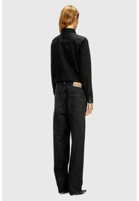 Giacca in denim nero con un design strutturato, abbinata a jeans neri a vita alta. Presenta tasche posteriori e un'etichetta sulla cintura.