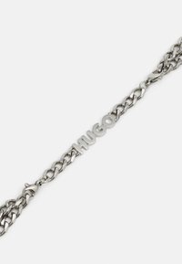 Bracelet chaîne en argent avec de grosses mailles et les lettres "HUGO" en design central sur fond blanc.