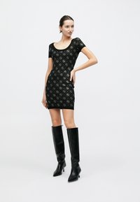 Μαύρο εφαρμοστό φόρεμα με στρογγυλή λαιμόκοψη, διακοσμημένο με επαναλαμβανόμενο γεωμετρικό μοτίβο. Συνδυασμένο με ψηλές, γυαλιστερές μαύρες μπότες μέχρι το γόνατο.