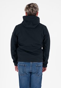 Zwarte hoodie-jack met een gestructureerde afwerking, voorzien van naden en zijzakken, gecombineerd met blauwe denim jeans. Achteraanzicht weergegeven.