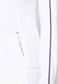 Camicia bianca a maniche lunghe caratterizzata da una texture liscia, design aderente, una striscia di accento grigia lungo la manica e un logo stampato in nero.