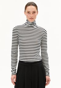 Schwarz-weißer gestreifter Rollkragenpullover aus weichem Stoff, mit langen Ärmeln und taillierter Passform, kombiniert mit hochtaillierten schwarzen Hosen.