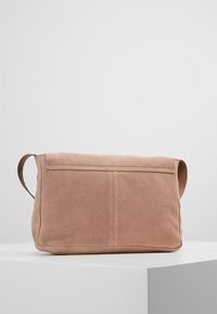 Růžová nubuková kabelka s plochým designem, vybavená jedním úchopem a jemnými švy na přední straně. Hladká textura, minimalistický styl.