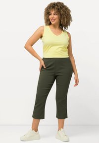 Débardeur jaune à col en V associé à un pantalon cropped vert foncé et des baskets blanches. Matière légère, design ajusté et texture lisse.
