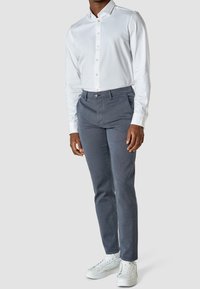 Vit skjorta med knappar, grå skräddarsydda byxor och vita sneakers. Outfitten har ett smidigt tyg och en slim fit-design.