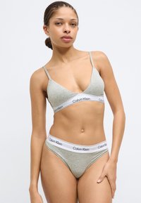 Ανοιχτό γκρι βαμβακερό σουτιέν bralette και τάνγκα που ταιριάζουν με λευκές ταινίες λογότυπου Calvin Klein. Οι τιράντες είναι λεπτές· το ύφασμα έχει ομαλή υφή.