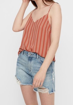 Femme portant un haut sans manches orange rouille à rayures verticales blanches et un short en jean bleu clair déchiré.