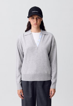 Maglione di lana grigio con scollo a colletto, con dettagli a bottoni a righe blu e bianche, abbinato a pantaloni larghi grigio scuro.