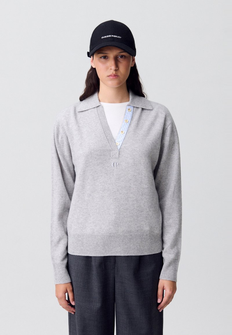 Maglione di lana grigio con scollo a colletto, con dettagli a bottoni a righe blu e bianche, abbinato a pantaloni larghi grigio scuro.