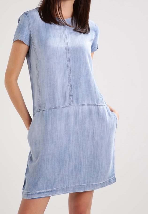 Vaate sinisestä denimistä, jossa on lyhyet hihat, pyöreä pääntie, etutaskut ja näkyvät ompeluseikat, valmistettu pehmeästä puuvillamateriaalista.