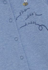 Hellesblaues Baumwoll-Overall mit einer gestickten Biene über dem Text "the bee's knees" in dunkler blauer Stickerei und Druckknopfverschluss.