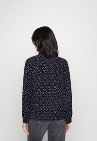 Long-sleeve shirt in navy fabric with white polka dots, button cuffs, and a classic collar. Smooth texture, relaxed fit, back view.