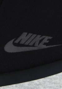 Μαύρο ύφασμα με εμφανές γκρι λογότυπο της Nike. Το υλικό έχει ραβδωτή υφή, με μια λε ία περιοχή στο κάτω μέρος.