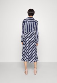 Tmavě modré a bílé proužkované šaty s dlouhým rukávem, s přiléhavým pasem a splývavou sukní. Mají límec a manžety na knoflíky.