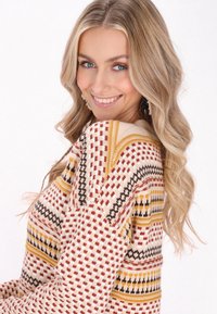 Maglione a maglia con una base crema, caratterizzato da motivi geometrici rossi, neri e gialli. Maniche lunghe e vestibilità rilassata con tessuto testurizzato.