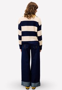 Navy- und cremefarbener gestreifter Pullover mit lockerer Passform, kombiniert mit weit geschnittenen, dunklen Jeans aus Denim mit umgeschlagenen Säumen und sichtbaren Nähten.