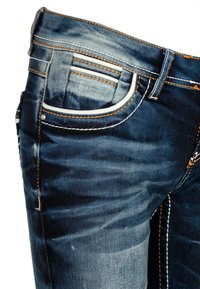 Dunkelblaue Jeans aus Denim mit einem verblassten Design. Zu den Merkmalen gehören orangefarbene Nähte, eine Fronttasche und schräg geschnittene Details an den Gesäßtaschen.